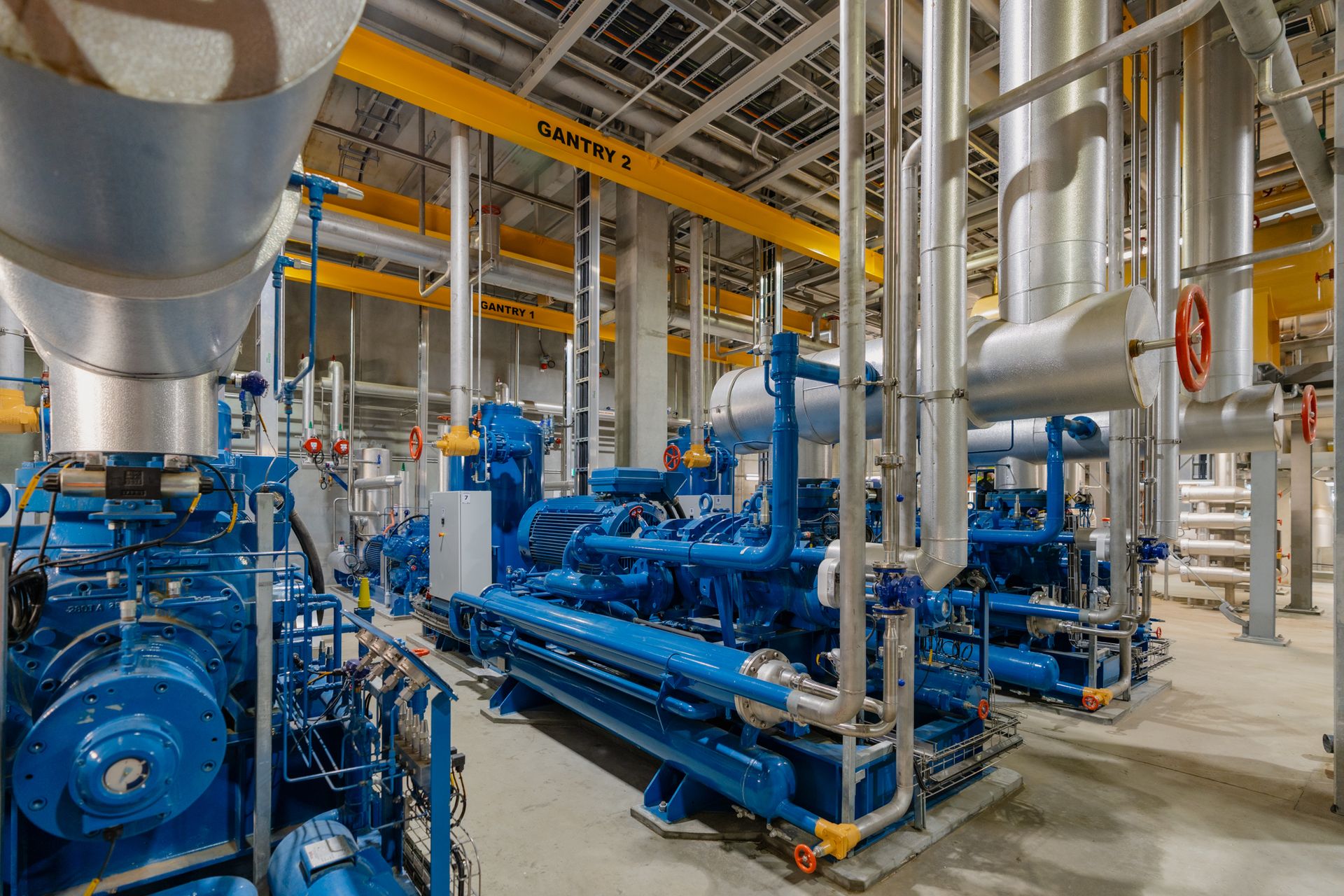 Refrigeration engine room with NH3 and CO2 cascade compressors under blue gantry